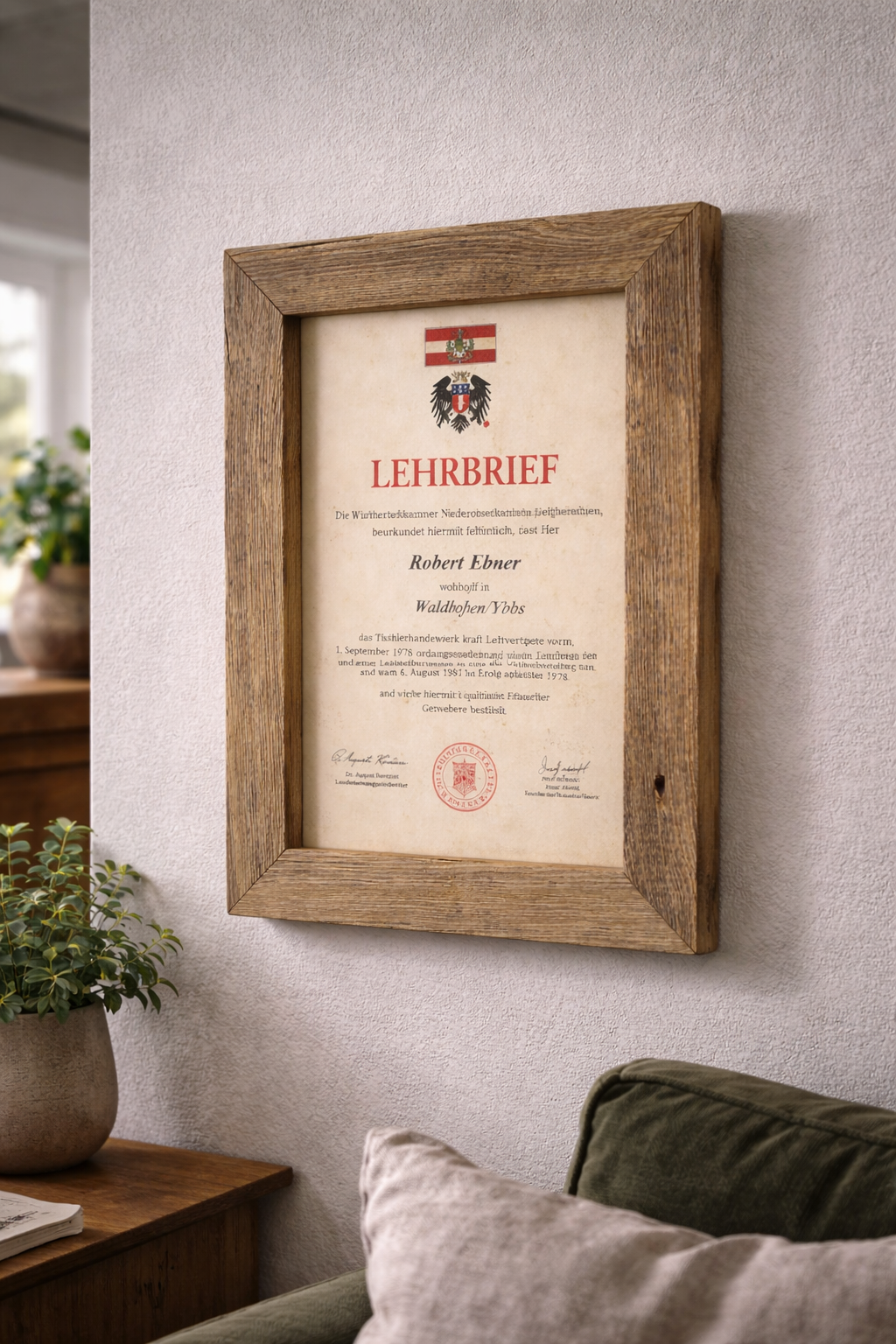 Altholzbilderrahmen mit einer Urkunde als Wanddeko vor einem Sofa. 