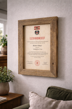 Altholzbilderrahmen mit einer Urkunde als Wanddeko vor einem Sofa. 