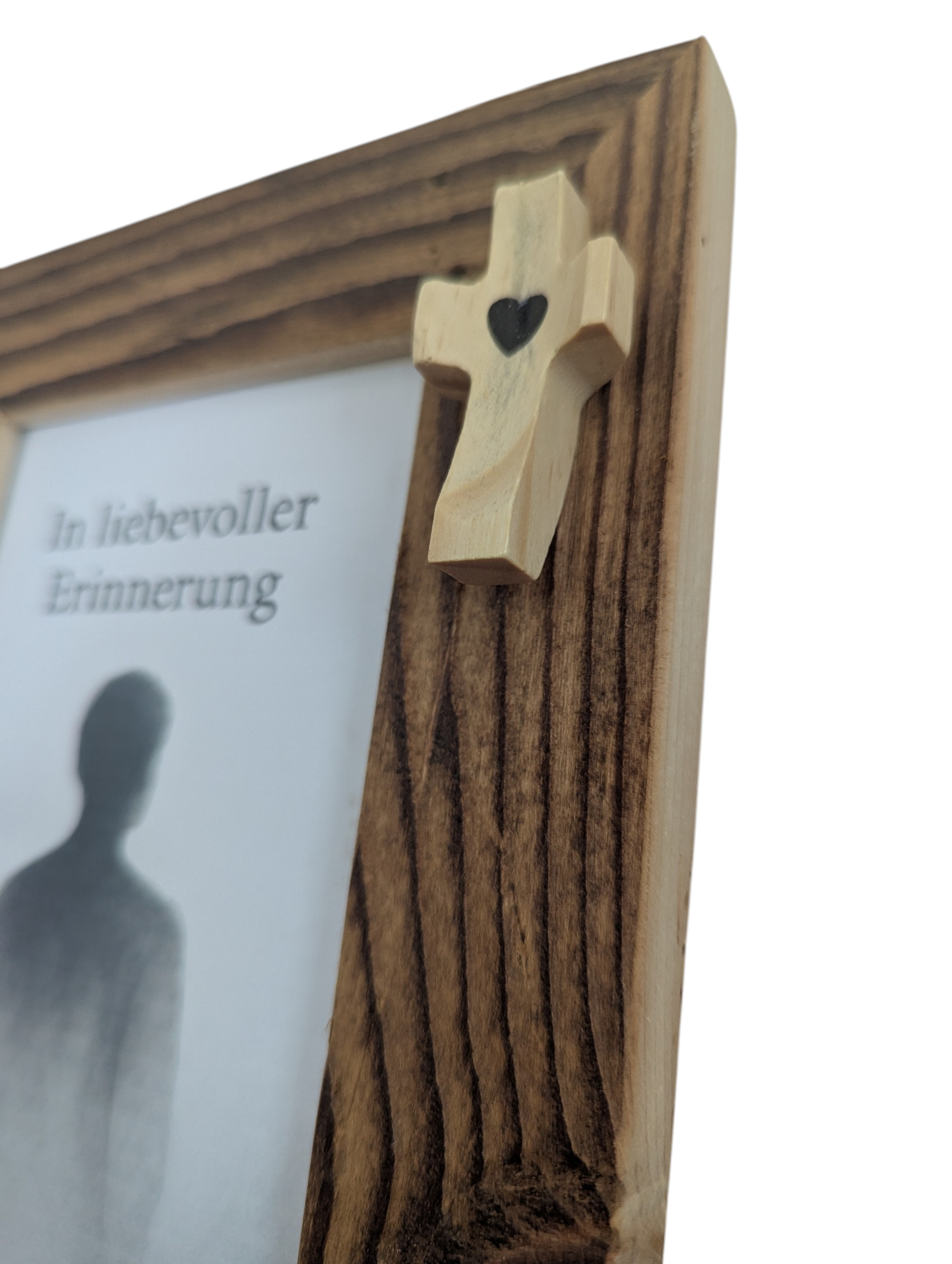 Detailaufnahme eines Bilderrahmen aus Altholz in rustikalem Stil zur Erinnerung an Verstorbene mit hellem Kreuz in der oberen, rechten Ecke. 