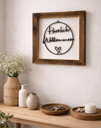 Bilderrahmen aus Altholz mit der Inschrift Herzlich Willkommen hängt an der Wand in einem modernen Eingangsbereich. 