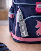 Handgemachter Schlüsselanhänger aus grauem Filz mit der Aufschrift Schutzengel auf einer Schultasche. 