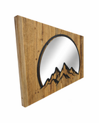 Seitenansicht eines Spiegels mit Bergmotiv aus Metall auf Altholz. 