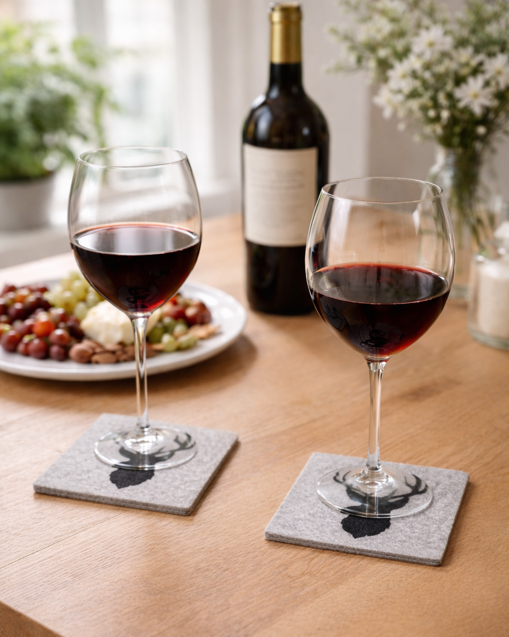 Weingläser mit Rotwein auf alpikat Filzuntersetzer mit Hirschmotiv auf einem Esstisch. 