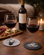 Weingläser gefüllt mit Rotwein auf grauen Untersetzern aus Filz mit Hirsch bzw.. Bergmotiv. 