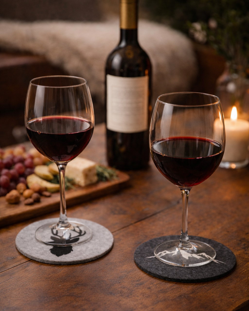 Weingläser gefüllt mit Rotwein auf grauen Untersetzern aus Filz mit Hirsch bzw.. Bergmotiv. 